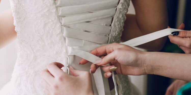 two women helping a bride to try a wedding dress on