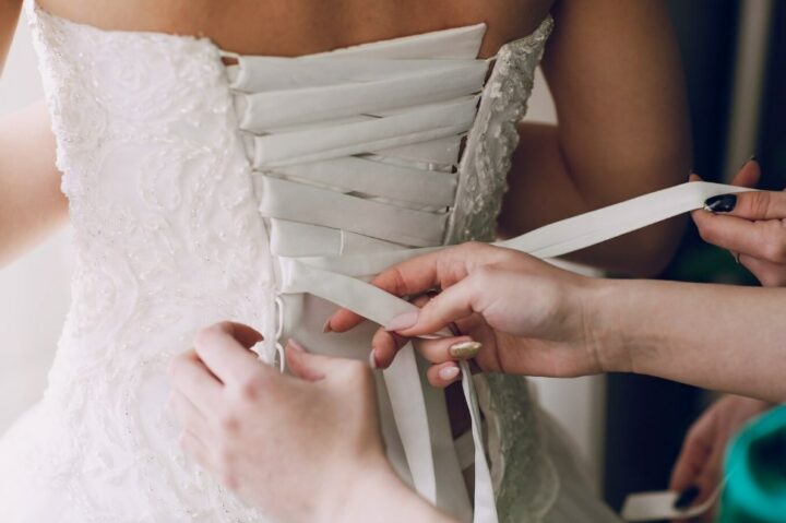 two women helping a bride to try a wedding dress on