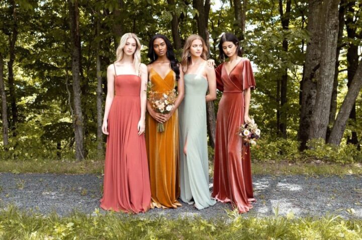 Several girls in dresses stand against the background of trees