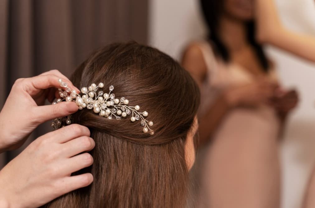 A hand fixing a pearl and crystal hairpiece in a bride's hair