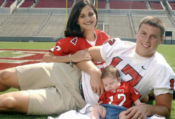 A family in sports jerseys on a football field, with a baby in a miniature jersey