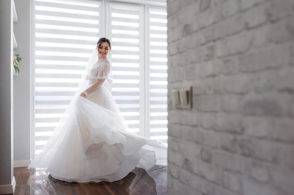 a woman in a white wedding dress in the room stands near the window and smiles