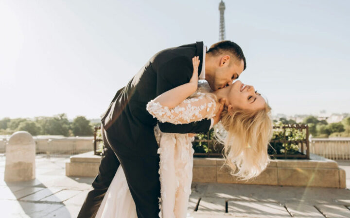 Couple kissing by the Eiffel Tower, bride in lace gown, groom in suit