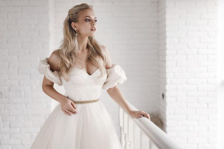 A bride in a white dress with puffed sleeves standing by a railing