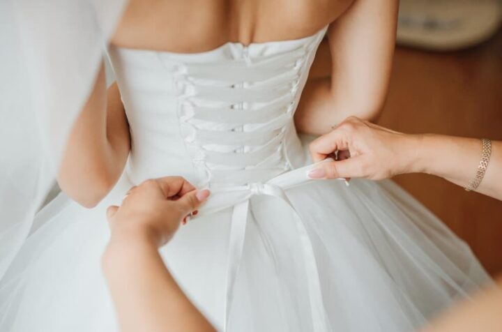 a close-up view of a person tying a bow on the bride’s wedding dress on the back