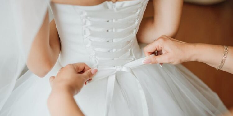 a close-up view of a person tying a bow on the bride’s wedding dress on the back