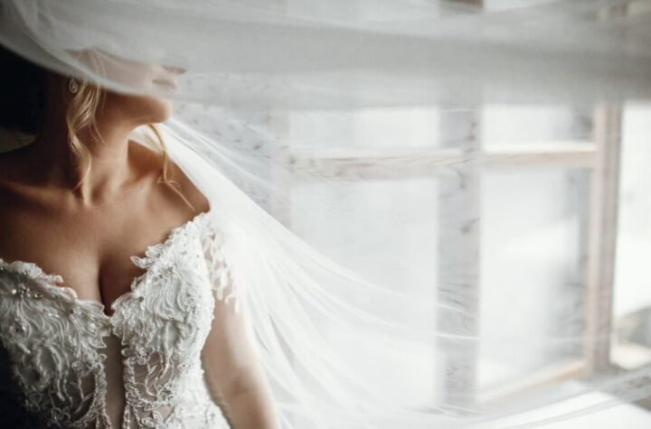 a close-up view of a woman in a white wedding dress and face closed with the veil