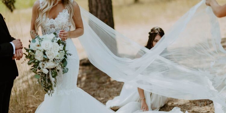 Bride in white dress and long veil with flowers in her hands