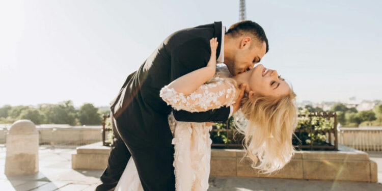 Couple kissing by the Eiffel Tower, bride in lace gown, groom in suit