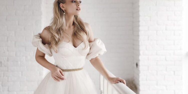 A bride in a white dress with puffed sleeves standing by a railing