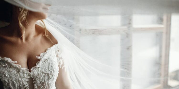 a close-up view of a woman in a white wedding dress and face closed with the veil